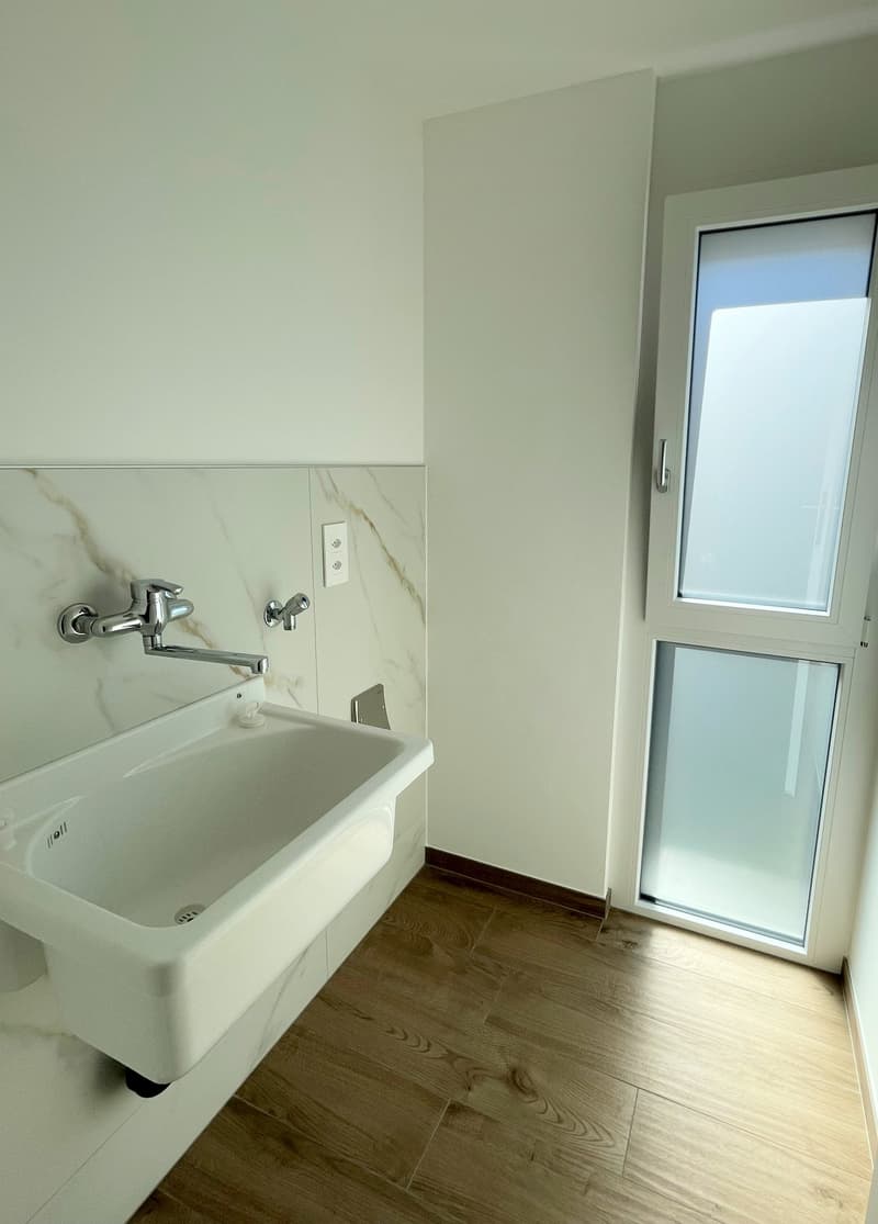 modern bathroom with white tiled walls, wooden floor, large sink, shower, and power outlet