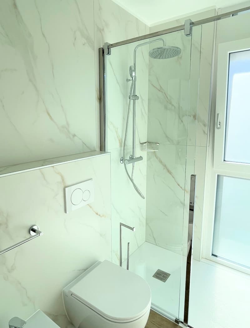 tiled walls, modern shower area with glass enclosure, shower head, shower rail, shower tray, toilet, and bidet.