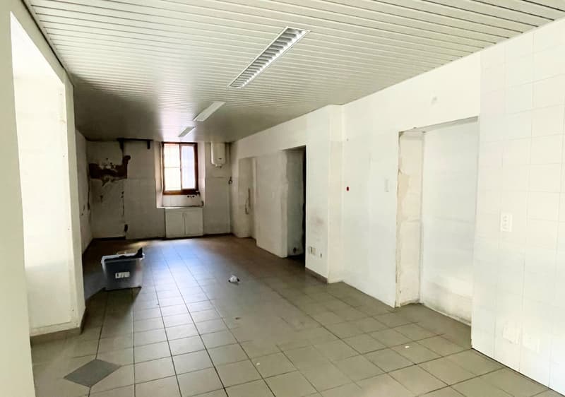 Empty room with white walls, tiled floor, ceiling with lights, small window, and a trash bin
