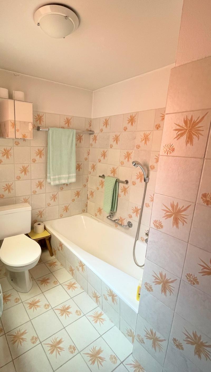 white tile walls, white bathtub, green towel, white toilet, a cabinet with mirrors