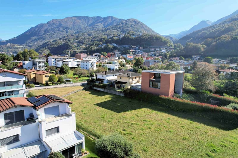 House with solar panels on the roof, large grassy field in front, elevated terrain with a wide view of the mountains.