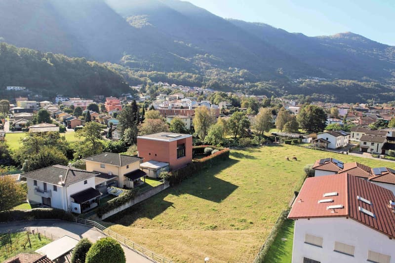 An aerial view of a neighborhood with mountains in the background, houses and a grassy field.