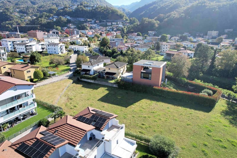 Aerial view of residential area with several houses, open field, solar panels on roofs, green surroundings