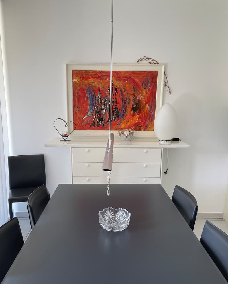 Dining room with a black table, black chairs, a white cabinet, a painting, and a lamp