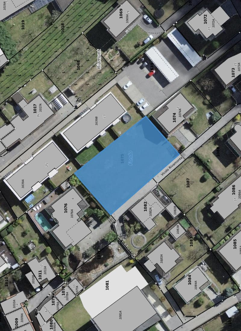 Aerial view of a residential area with multiple buildings, a large blue-marked plot of land, and surrounding streets and parking areas.