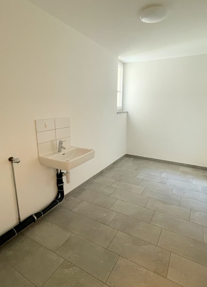 Empty room with white walls, tiled floor, a sink with faucet, and a window.