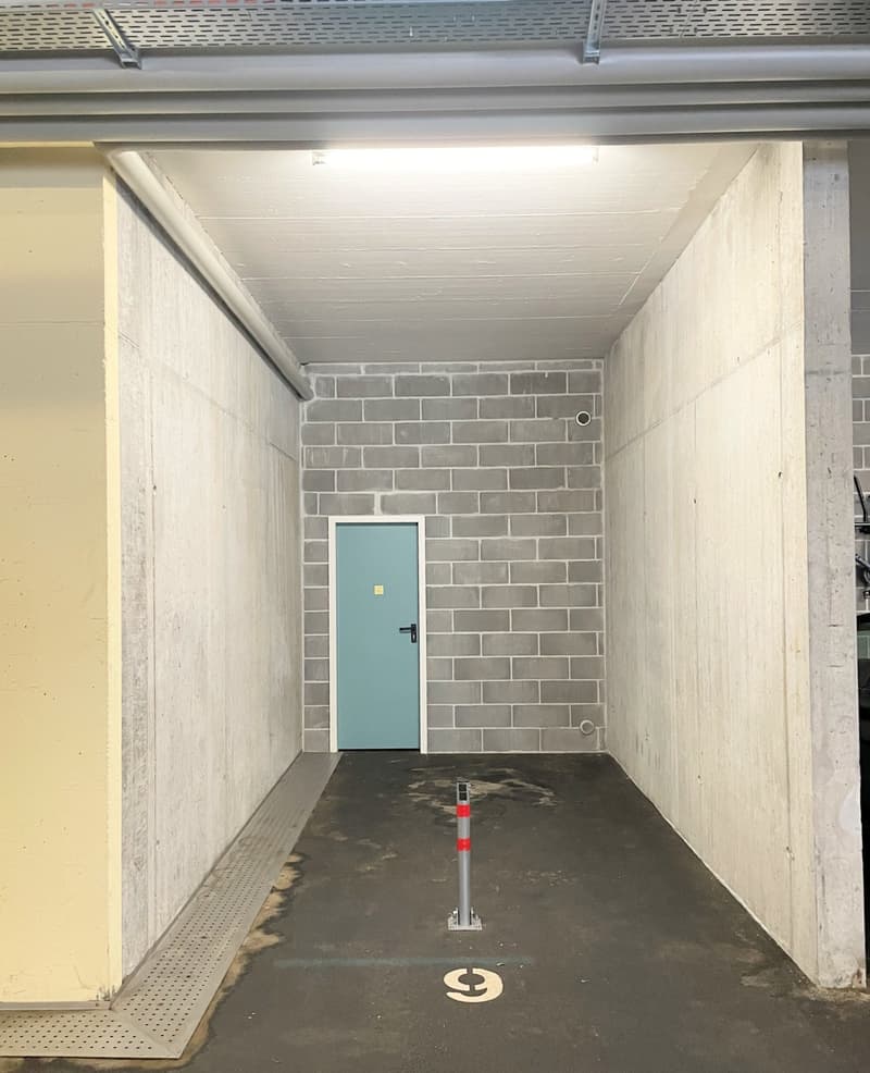 Empty parking area with a single parking spot marked with a number 9, walls made of concrete and brick, a door, and a ceiling with a light