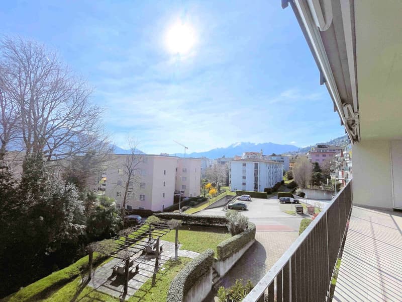 balcony with railing, view of a parking lot, trees, bushes, buildings, mountains