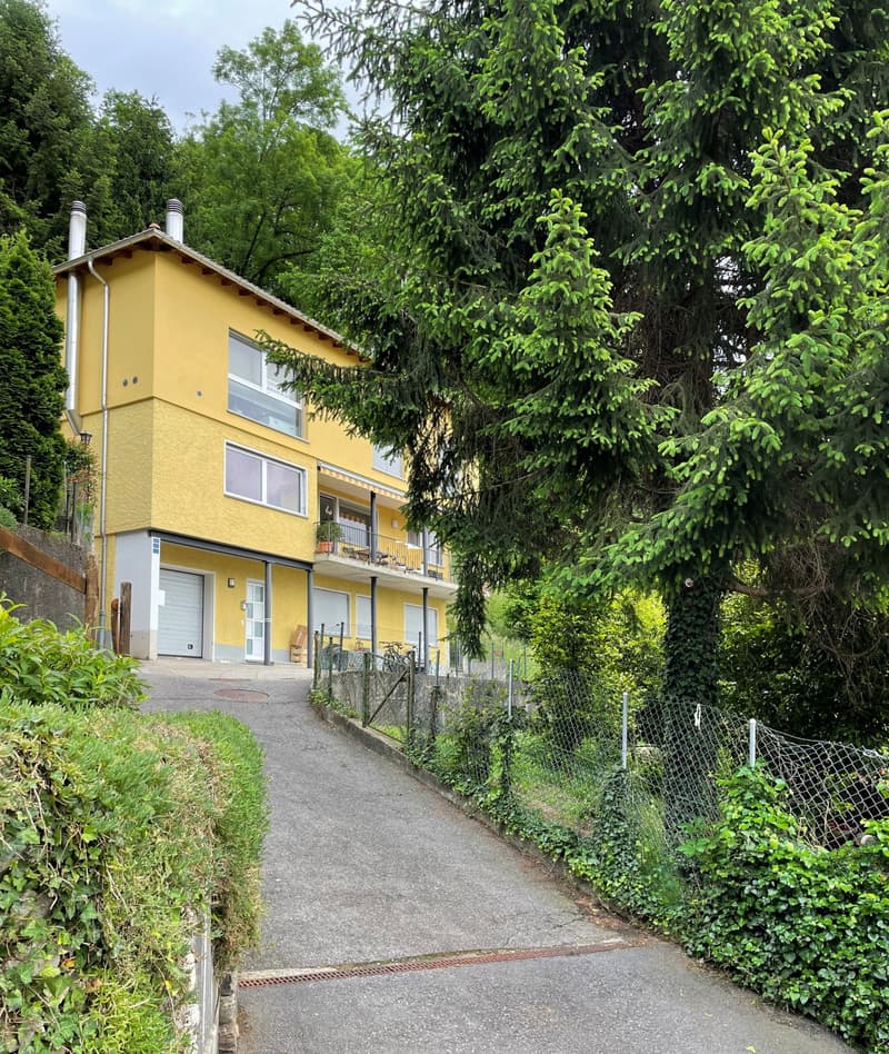 2 story house, yellow exterior, 2 garages, driveway, balcony, trees, plants