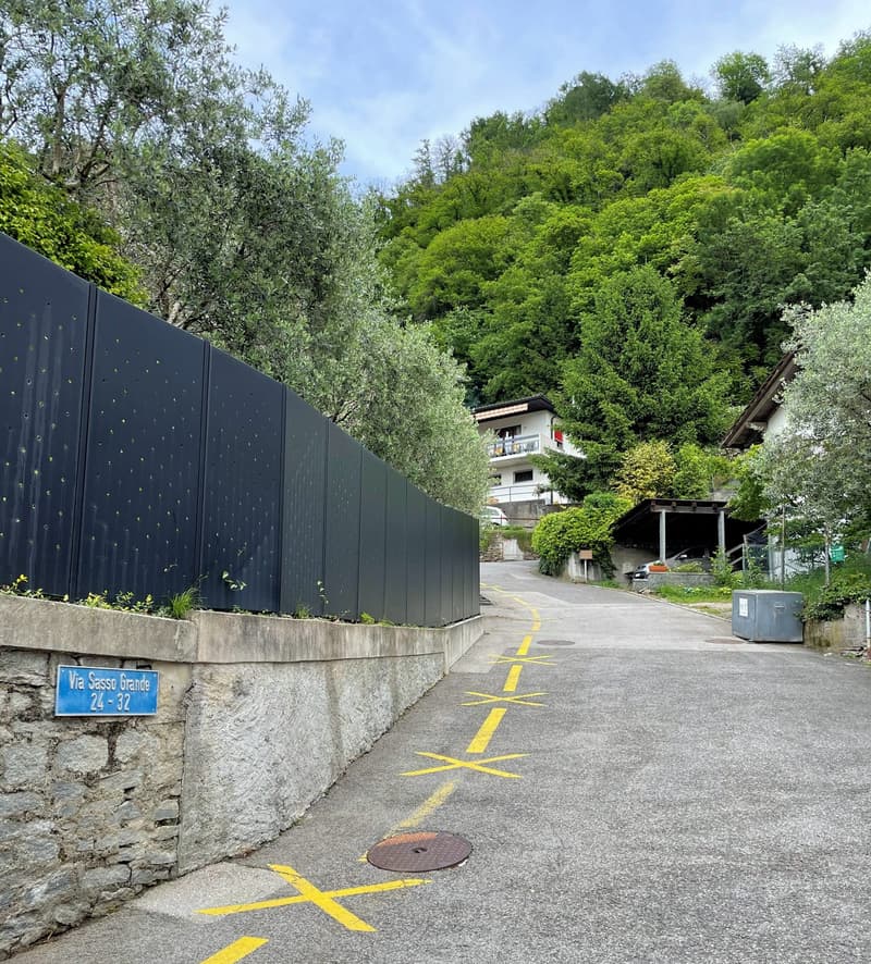road with yellow markings, stone wall, black fence, sign indicating parking spaces