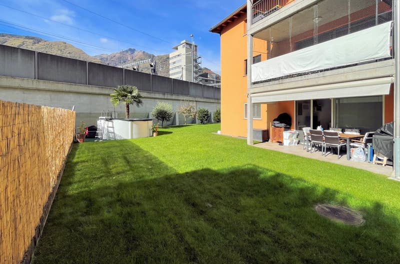 green lawn, wooden fence, palm tree, outdoor dining set, storage boxes, orange building with balcony
