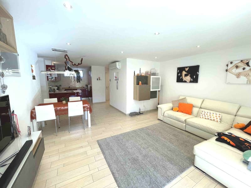white walls, wooden floor, white couch, dining table, TV, kitchen in the background