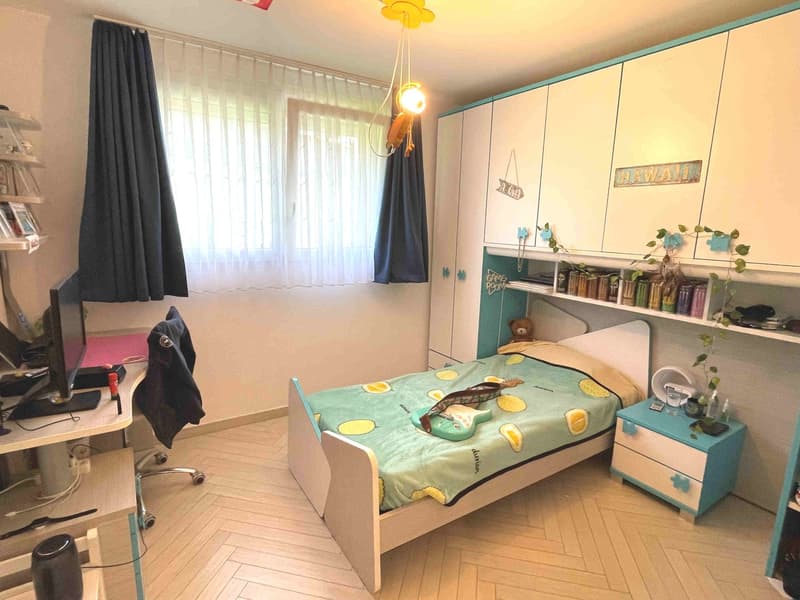 Bedroom with bed, desk, chair, shelves, and a guitar on the bed.