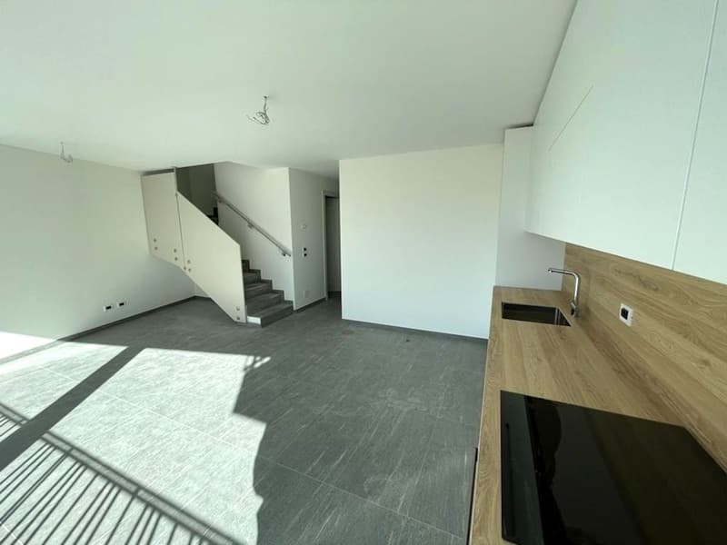 Empty room with white walls, gray floor, wooden countertop, sink, staircase