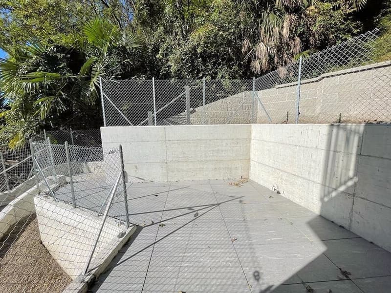 Concrete retaining wall, fenced area, paved ground, trees in the background