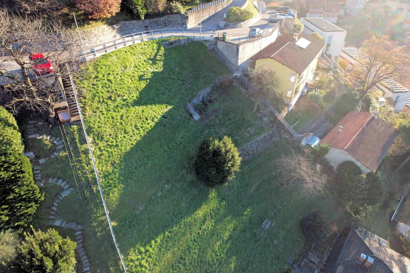 large grassy area, stone wall, trees, pathway, buildings in the background