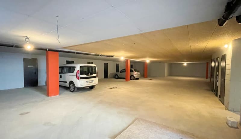 underground parking lot, two cars parked, white walls, orange pillars, ceiling lights