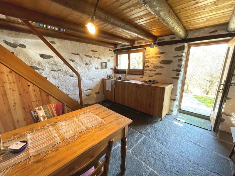 kitchen with wooden table, wooden cabinets, sink, stove, wooden ceiling, stone wall, open door