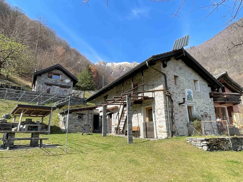 Stone house, solar panels on the roof, wooden porch, wooden ladder, garden, mountains in the background