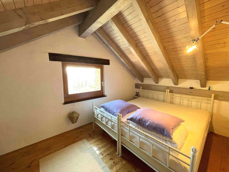 Bedroom with two single beds, wooden ceiling, white walls, wooden floor, window, lamp, rug