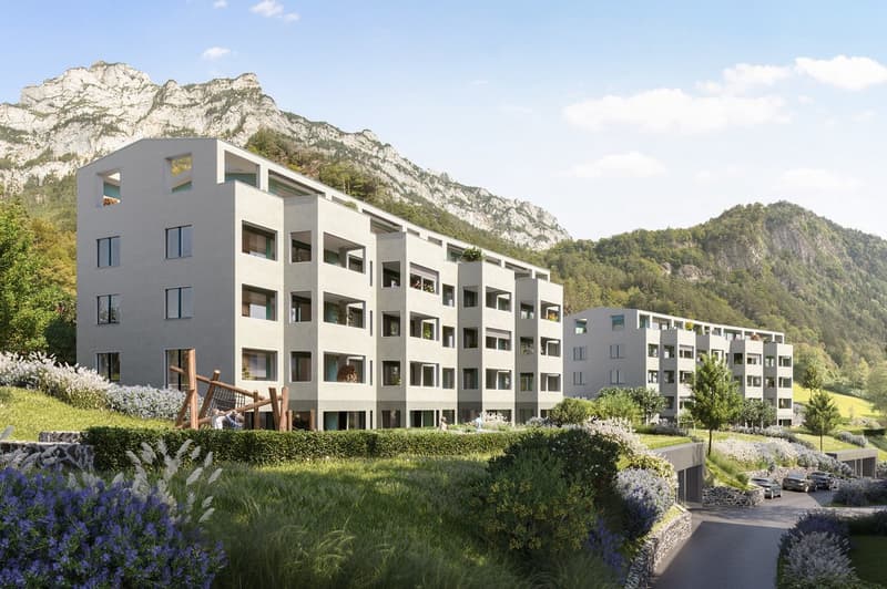 3-story building, white walls, large windows, balconies, green roof, garden, parking spots, grassy hills, mountains in the background