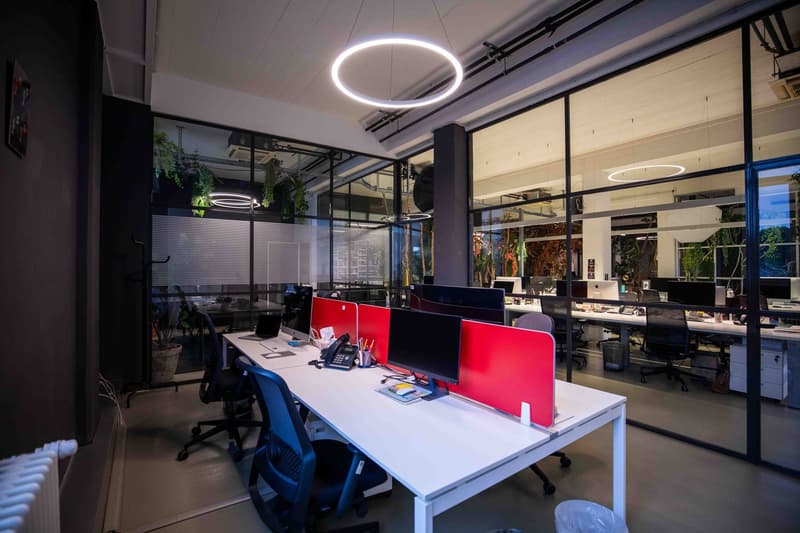 modern office with glass walls, white tables and chairs, monitors, plants, a large white circle lamp