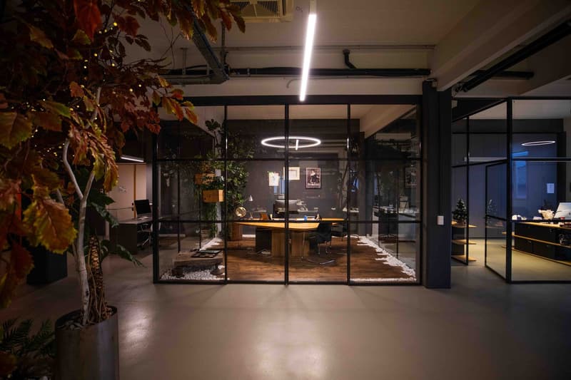 An office with glass walls, wooden flooring, modern furniture, a round desk, and plants