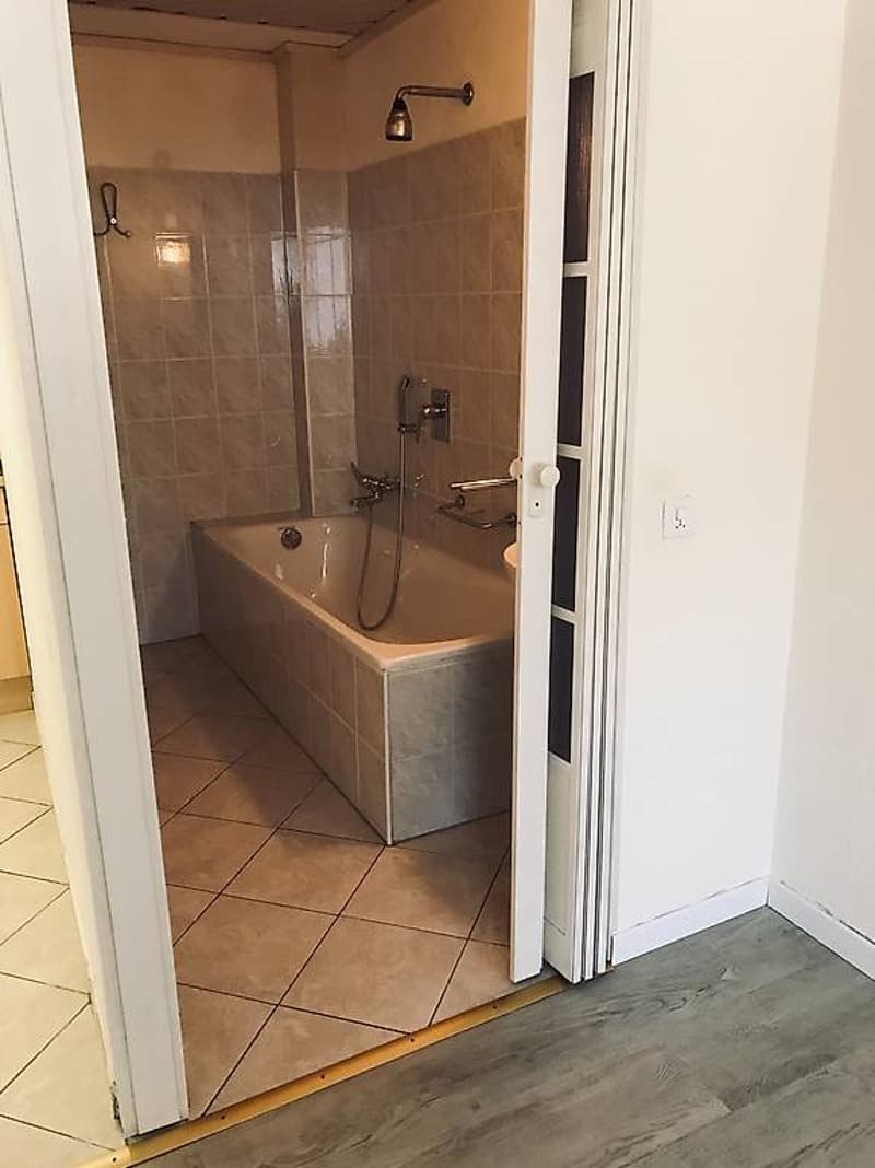 Bathroom with bathtub, shower attachment, tiled flooring, open door