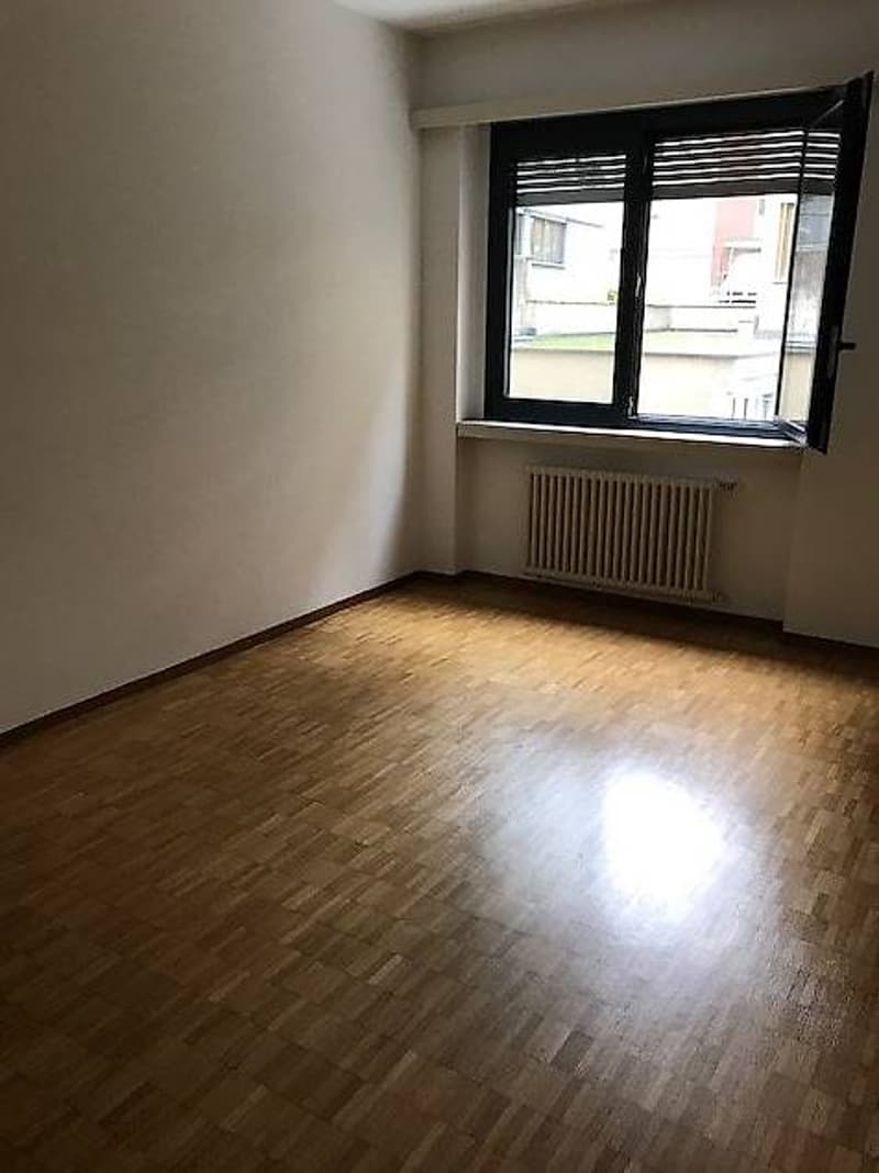 room with wooden floor, white walls, open window, radiator