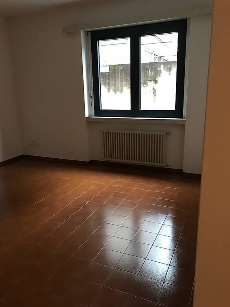 Empty room, white walls, brown tiles, a window with a white radiator underneath, white ceiling