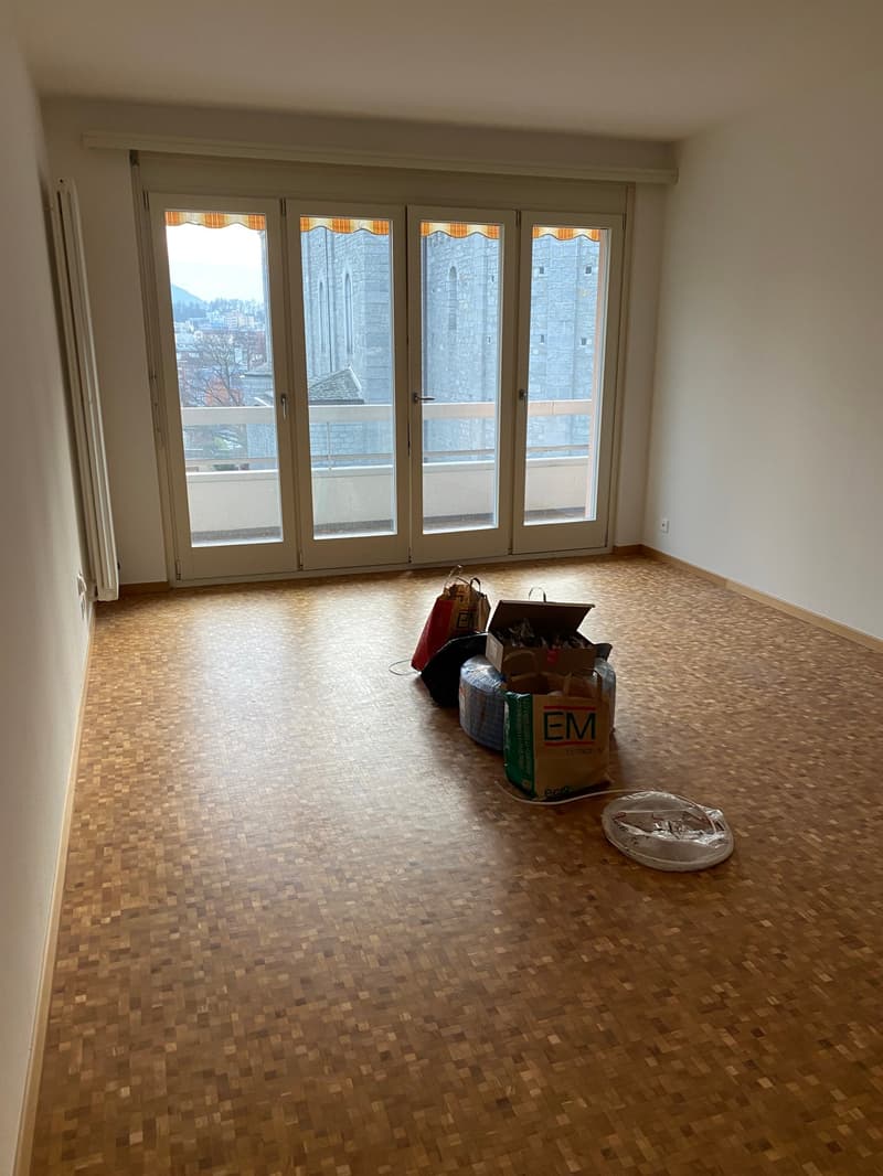 Empty room, wooden floor, sliding doors with a balcony view, electrical outlet, boxes on the floor