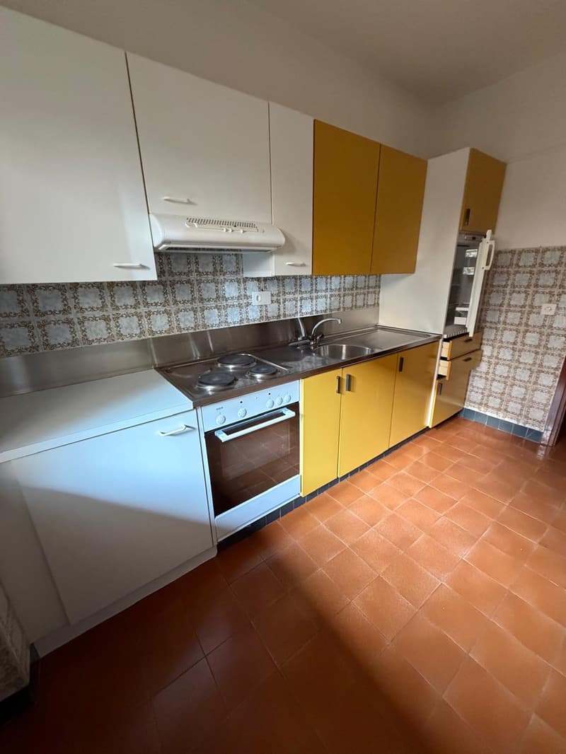 Modern kitchen with yellow cabinets, white countertop, gas stove, oven, sink, white tiled backsplash, tiled floor