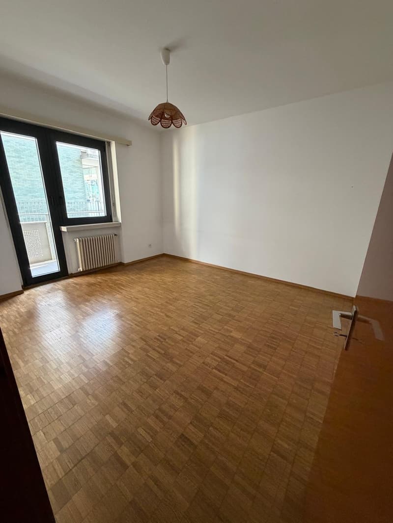 wooden floor, white walls, sliding glass door leading to balcony, white radiator, ceiling lamp