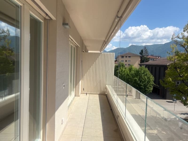 Balcony with glass railings, tiled floor, glass doors, mountains in the distance