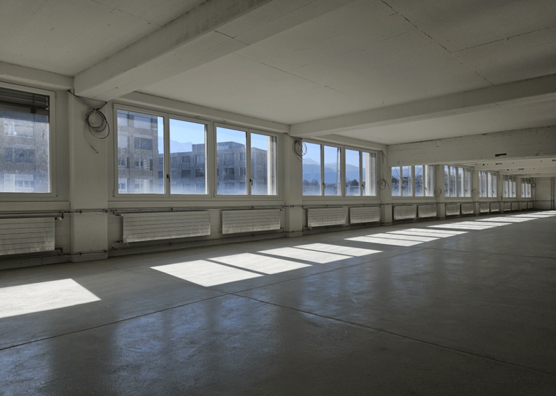 Empty large room with windows, concrete floor, no ceiling beams, white walls, heaters