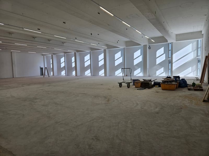 large empty room, white walls, white ceiling with exposed beams and lighting, glass windows with window coverings, trolley with materials and tools scattered on the floor