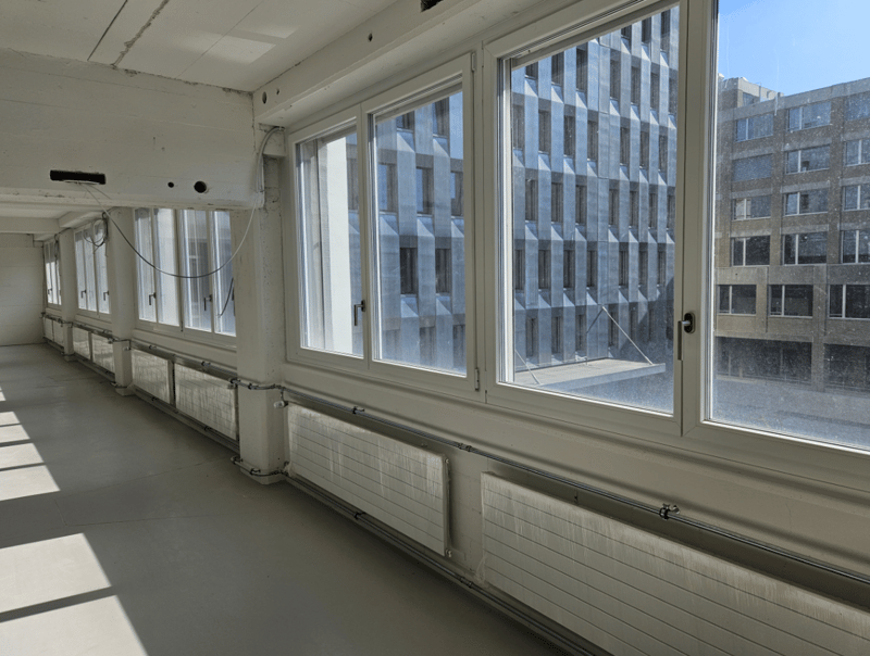 Empty office room with large windows, radiators, grey flooring