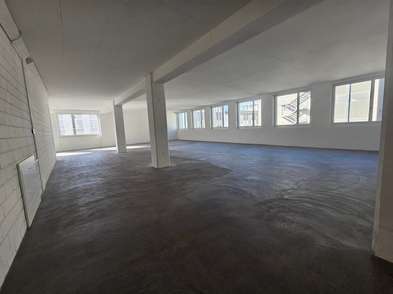 Open room with concrete floor, exposed ceiling, several windows, white walls