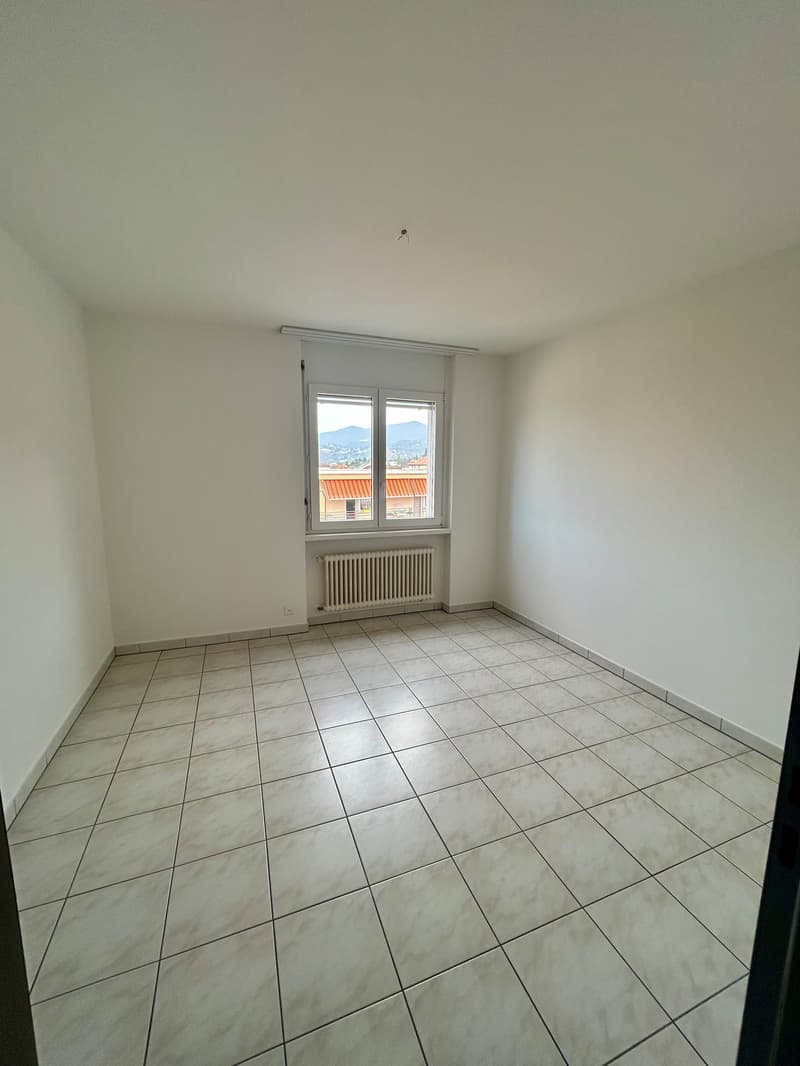 Spacious bedroom with tile flooring, large windows providing natural light, and a radiator for heating.