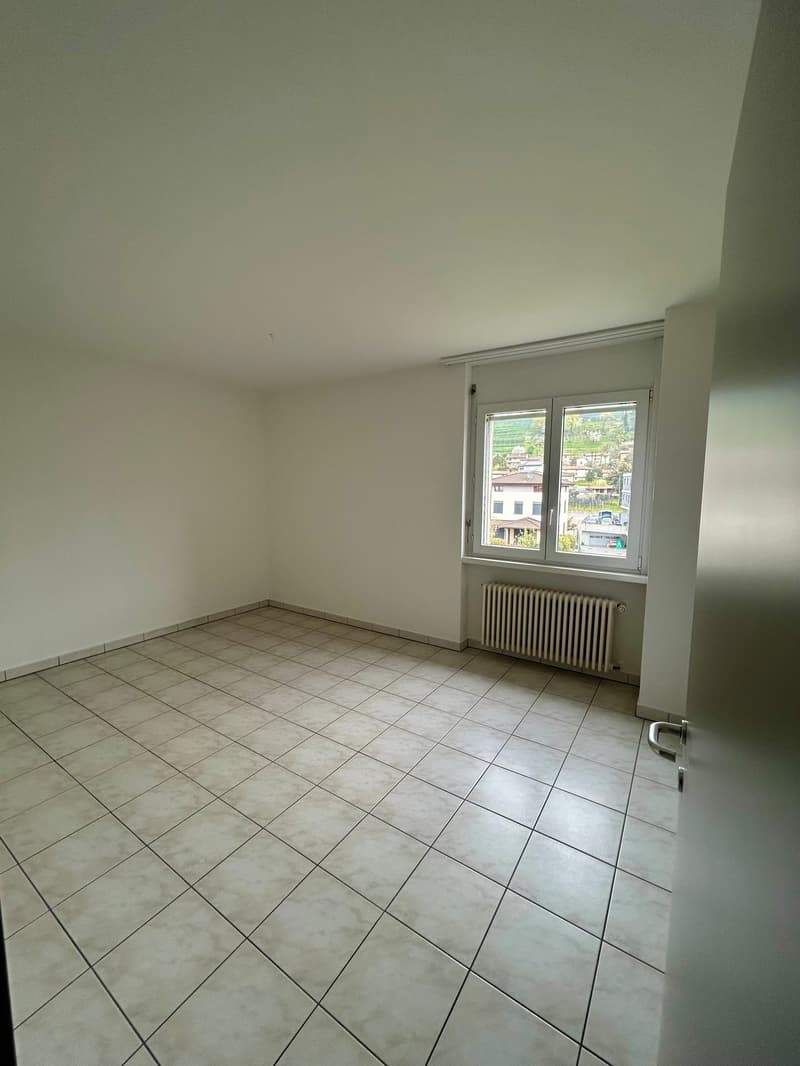Empty room with white walls, tiled floor, and a window overlooking the outside.
