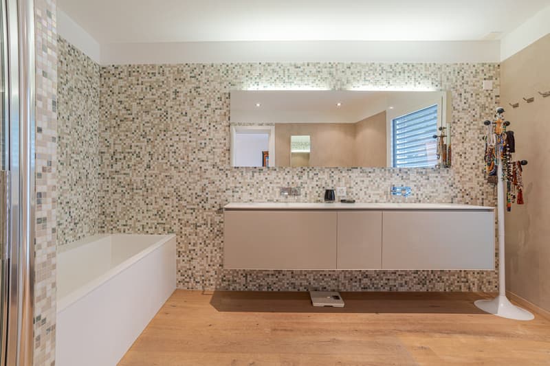 Modern bathroom with tile walls, bathtub, countertop sink, large mirror, wooden floor
