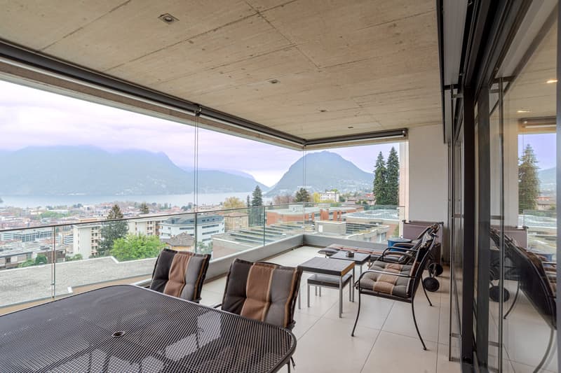 modern balcony with table, chairs, large glass windows, stunning lake and mountain view