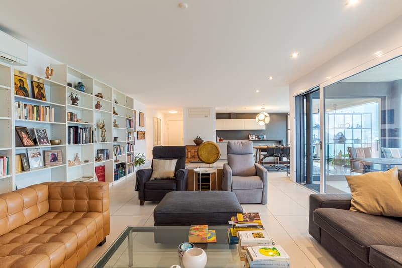 living room, modern style, white walls, large white bookshelf, brown leather couch, glass table, white tiled floor, sliding glass doors