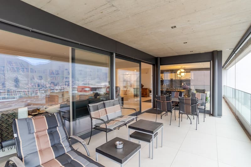 Outdoor terrace with white tiles, large sliding glass doors, reclining chairs, tables, scenic mountain view