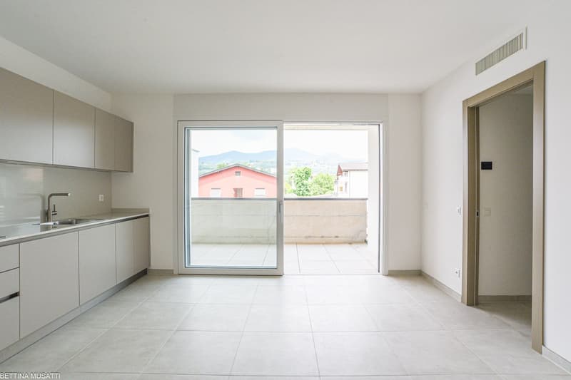 Modern kitchen with white tiled flooring, white cabinets, stainless steel sink, faucet, sliding glass door to balcony with outdoor view, open layout