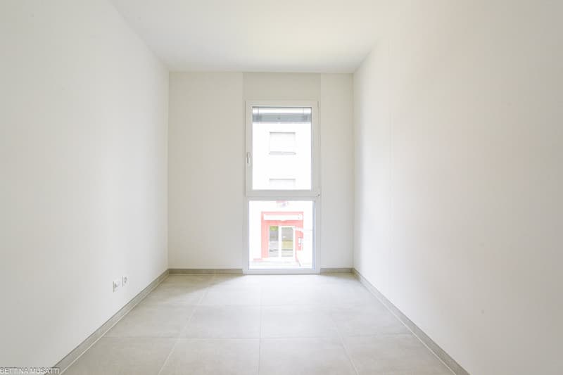 Empty room with tiled floor and white walls, view through a door to a building outside.
