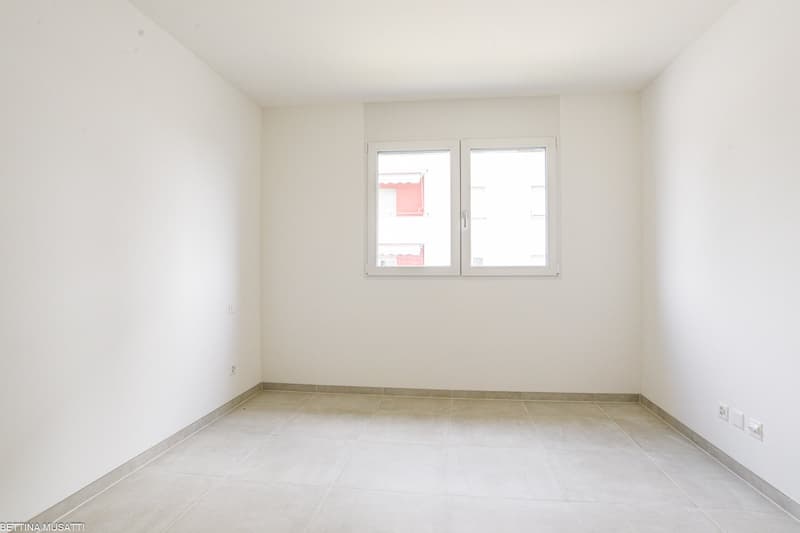 An empty room with white walls, tiled floor, white windows, a power outlet, and a water outlet