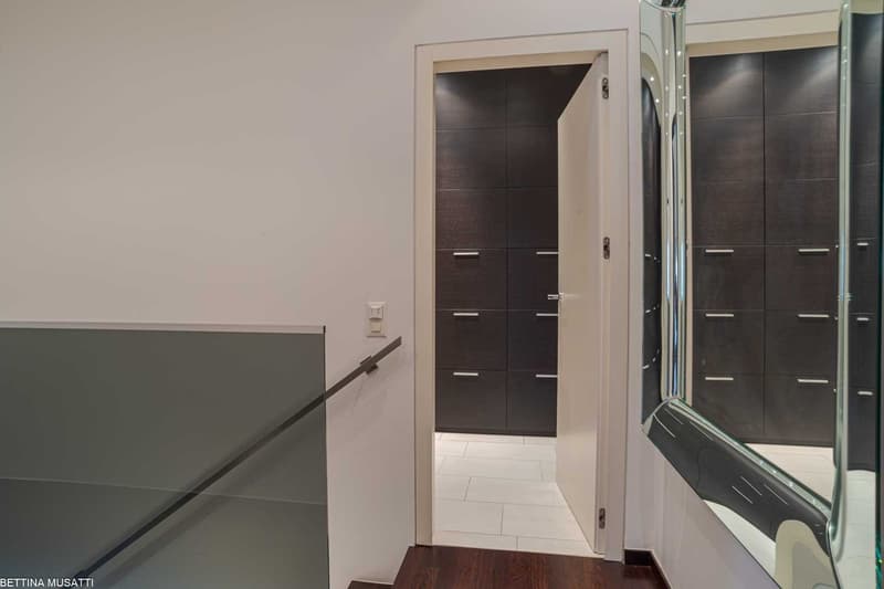 Glass railing, white walls, white tile floor, wooden door, mirror, wooden floor, multiple storage drawers