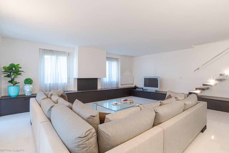 living room, white walls, large grey sofa, glass coffee table, two plants, windows with white curtains, white tiles, television