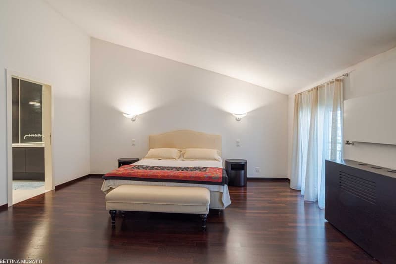 wooden floor, double bed, cream-colored bedding, 2 side tables, bench at foot of bed, white walls, ceiling-mounted wall lights, white curtains
